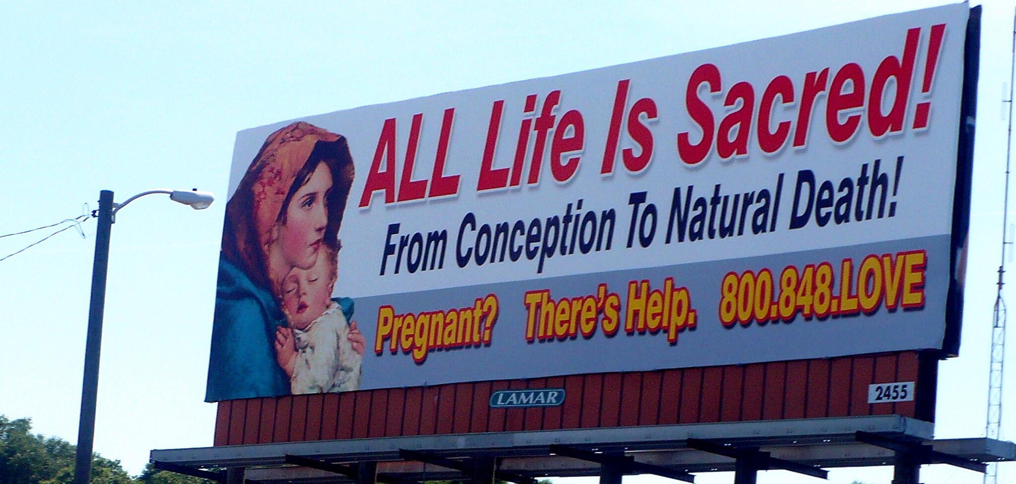 a billboard that says "All life is Sacred! From conception to natural death! Pregnant? There's Help. 800.748.LOVE"
