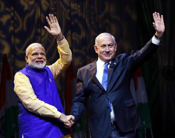Narendra Modi and Benjamin Netanyahu shaking hands and waving into the crowd.