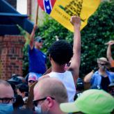 Pro-confederacy protestor holds up a confederate flag, a counter-protestor raises a fist in response.