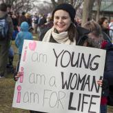 A white woman holding a sign saying "I am young, I am a woman, I am FOR life"