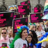 People in a protest wearing rainbow wigs, holding signs that say "love is a human right"