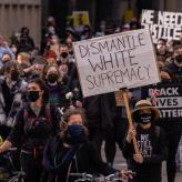 Protestors walking the street, one protestor holding a sign that says "Dismantle White Supremacy."