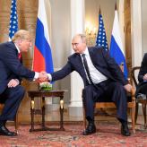Two men in suits leaning over a table shaking hands