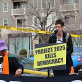 Two people on a podium with a board that reads "Project 2025 Kills Democracy"