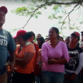 A group of people wearing red hats led by a man speaking with his hand raised.