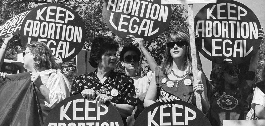 White women protesting, holding circular signs that say "Keep Abortion Legal"