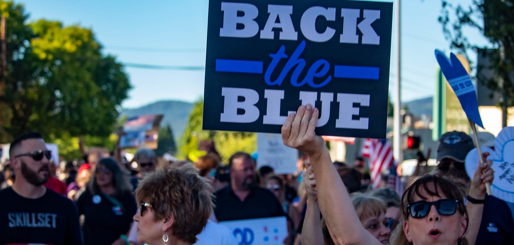 Protesters gathered. A woman holds up a sign that read Back the Blue.