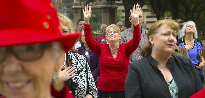 Older woman standing in crowd with both hands raised