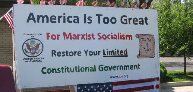 A sign that says "America is too great for marxist socialism. Restore your limited. Constitutional Government. www.jbs.org"