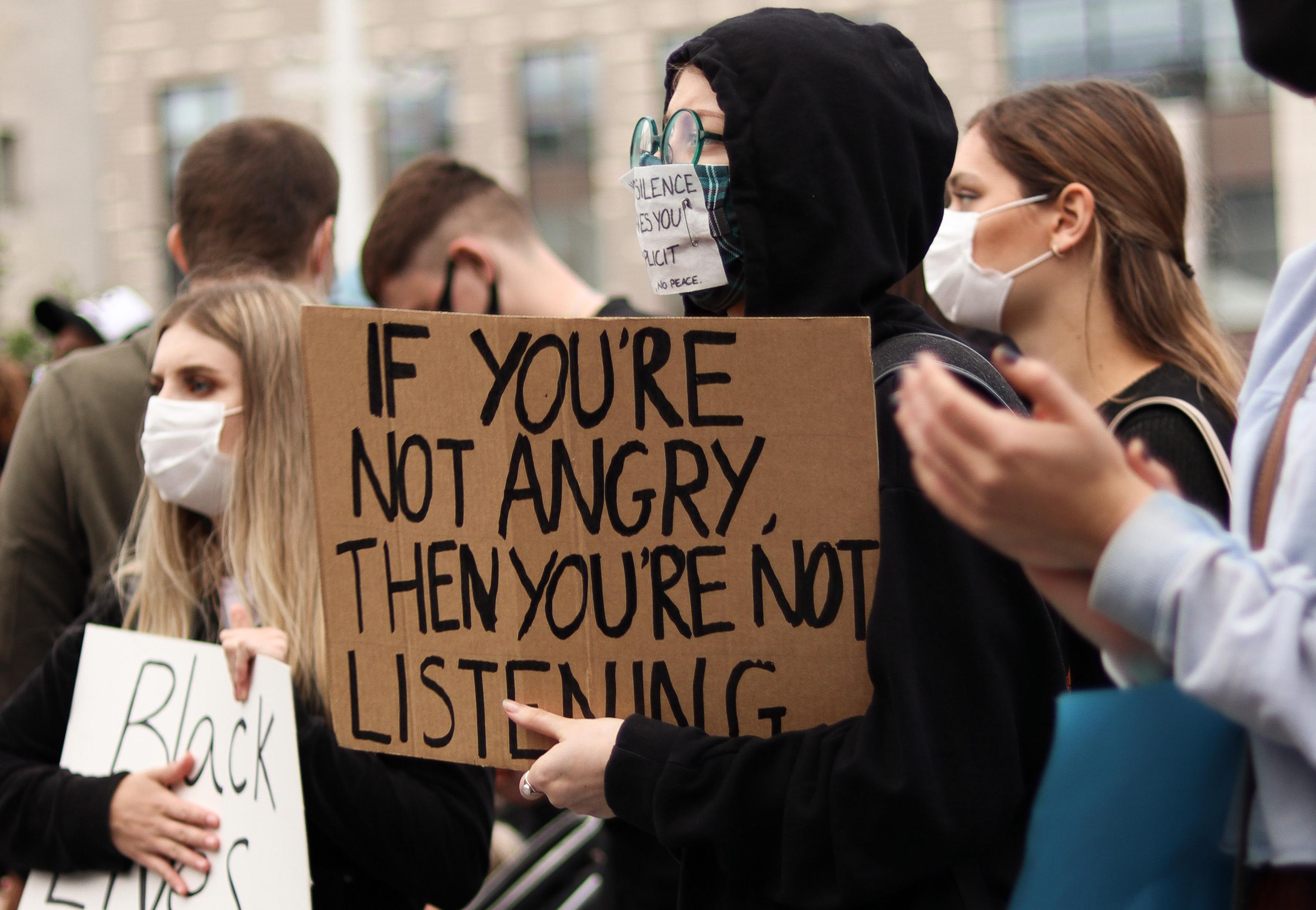 A person holding a sign that says "If you're not angry, then you're not listening."