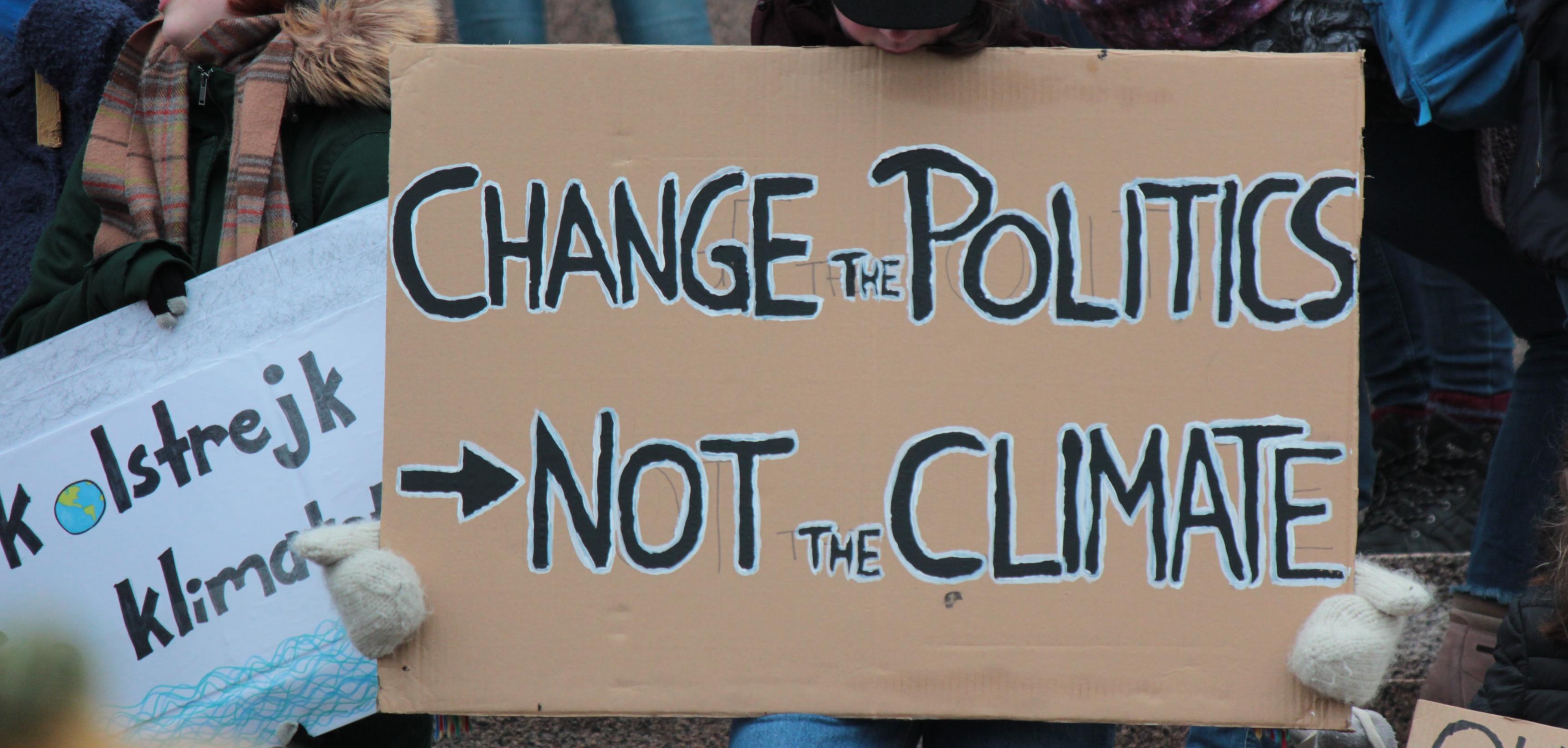 a protester with a sign that says "change the politics not the climate"