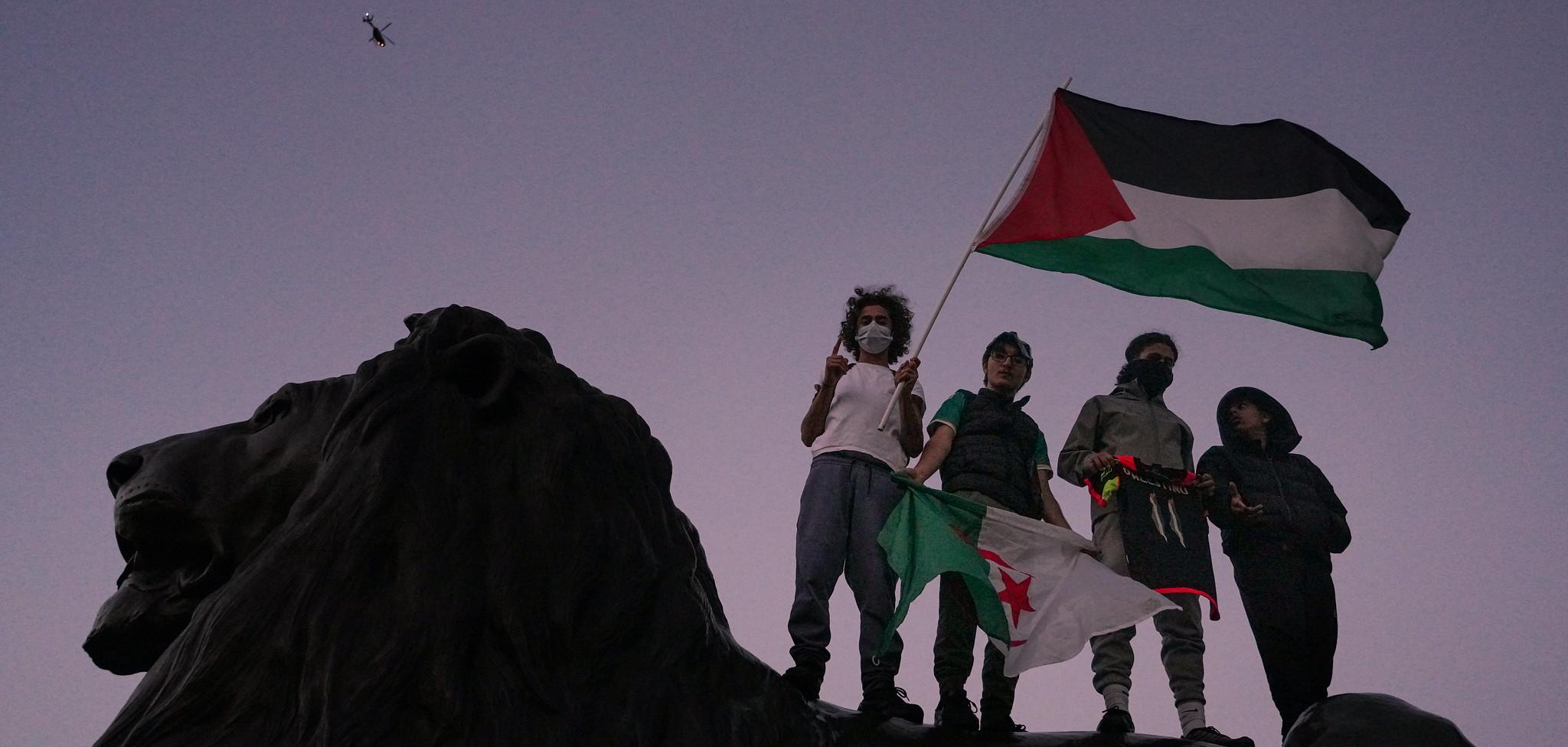 Four people carrying a Palestinian flag standing on a lion.