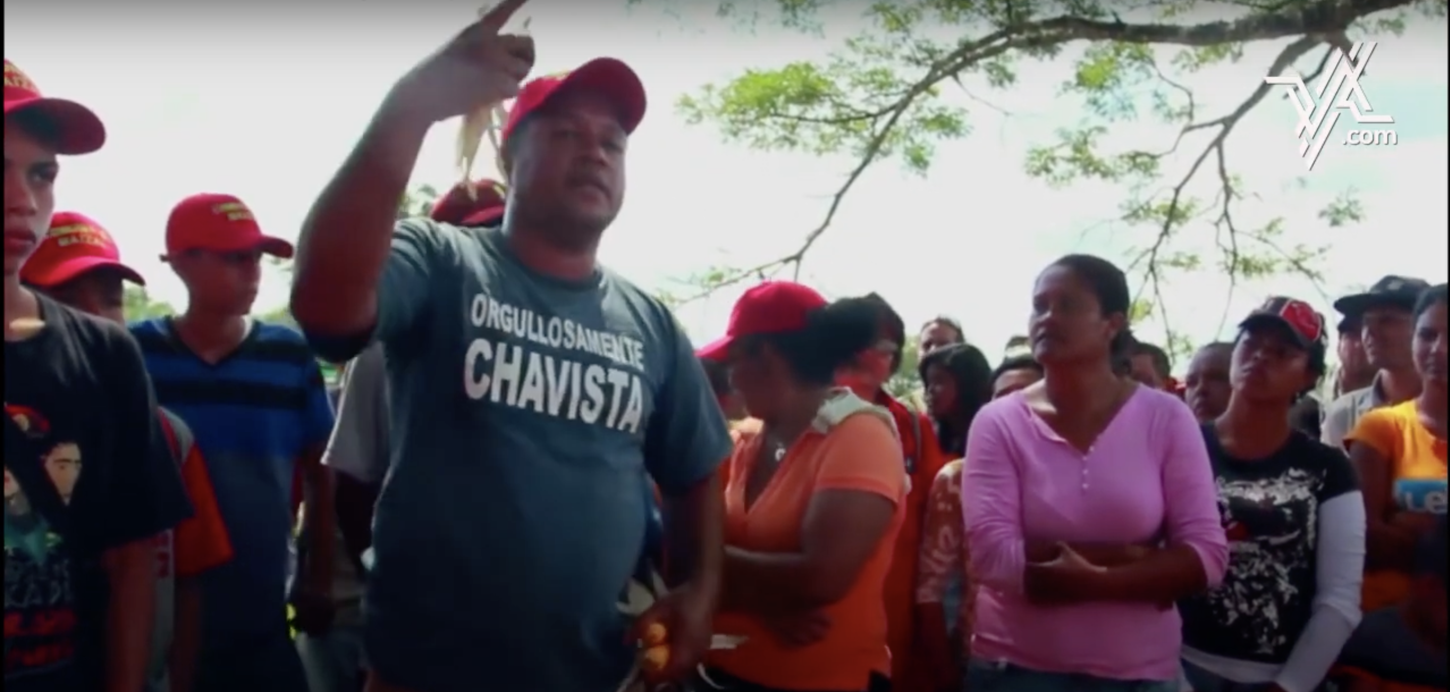 A group of people wearing red hats led by a man speaking with his hand raised.
