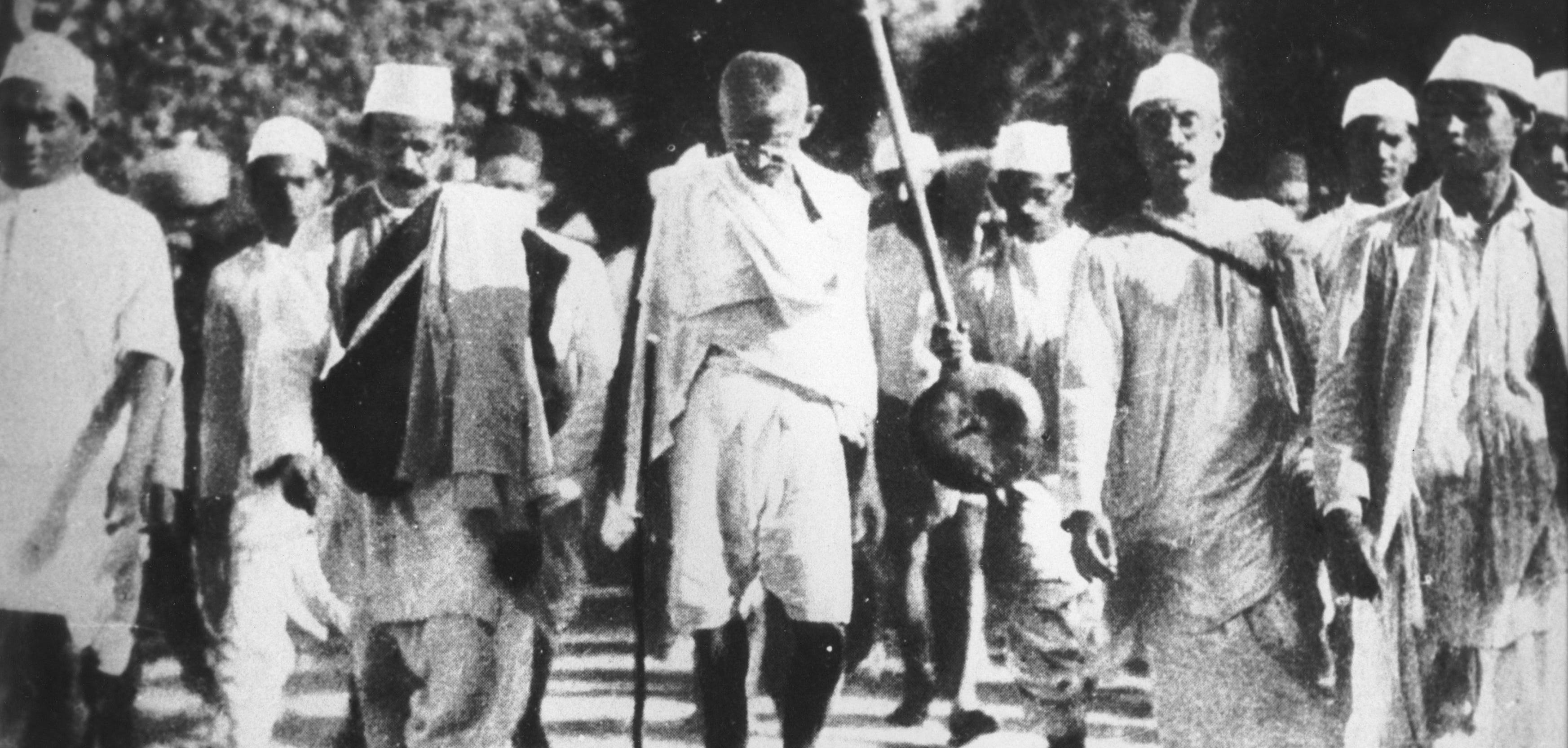 a black and white photo on people marching on the street, wearing hats and dhotis